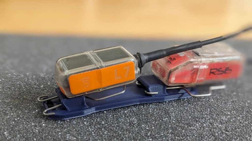 Two GPS trackers clipped to a 3D printed mount for tracking raptors during rehabilitation.